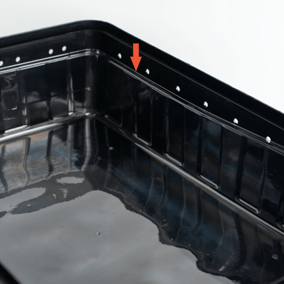 Close-up of the side of a black monotub showing drilled holes for ventilation, with an orange arrow indicating the clear liner nested inside of it. 